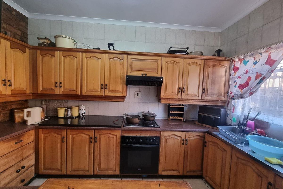 A functional kitchen featuring traditional wooden cabinetry, built-in oven with hob, extractor fan, and tiled backsplash with ample counter space.