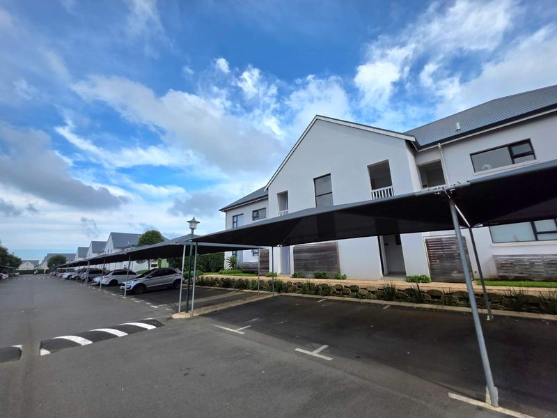 Exterior view of a townhouse complex featuring covered parking bays, paved driveway, and well-maintained building facades.