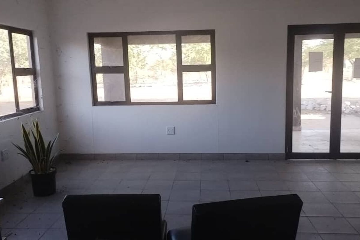 An empty, sunlit living area featuring tiled flooring, aluminium window frames, and a glass door leading to the exterior.