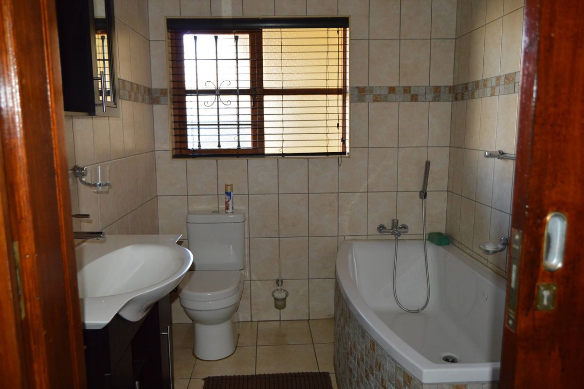A functional bathroom featuring a built-in bathtub with shower attachment, a vanity basin, and a toilet, finished with neutral wall and floor tiling.