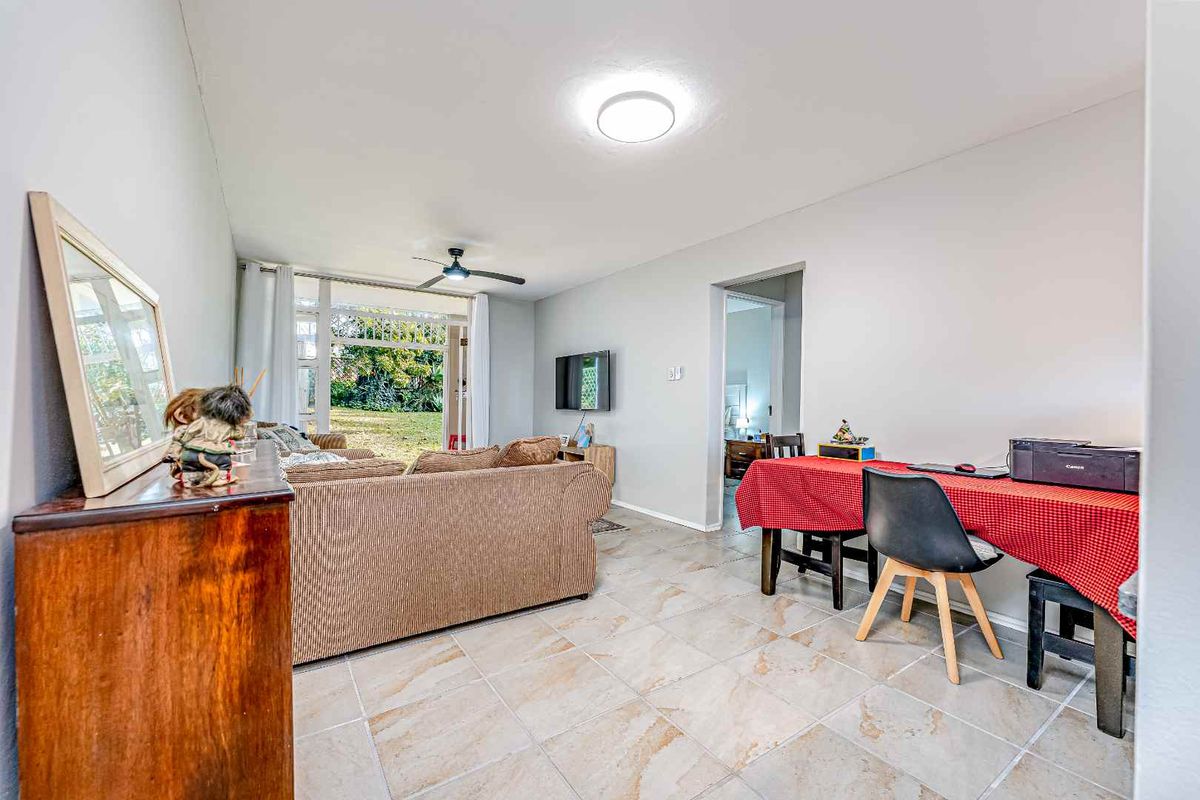 Spacious living area featuring neutral tiled flooring, a ceiling fan, and large sliding glass doors providing access to the outdoor garden space.