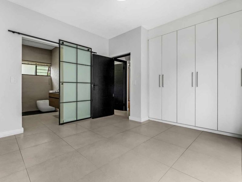 A spacious, modern bedroom featuring neutral tiled flooring, extensive built-in cabinetry, and a stylish sliding barn door leading to an en-suite bathroom.