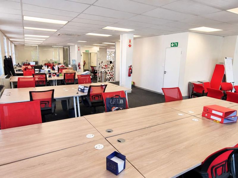 A spacious open-plan office area featuring suspended ceilings, recessed lighting, large windows for natural light, and integrated air conditioning.