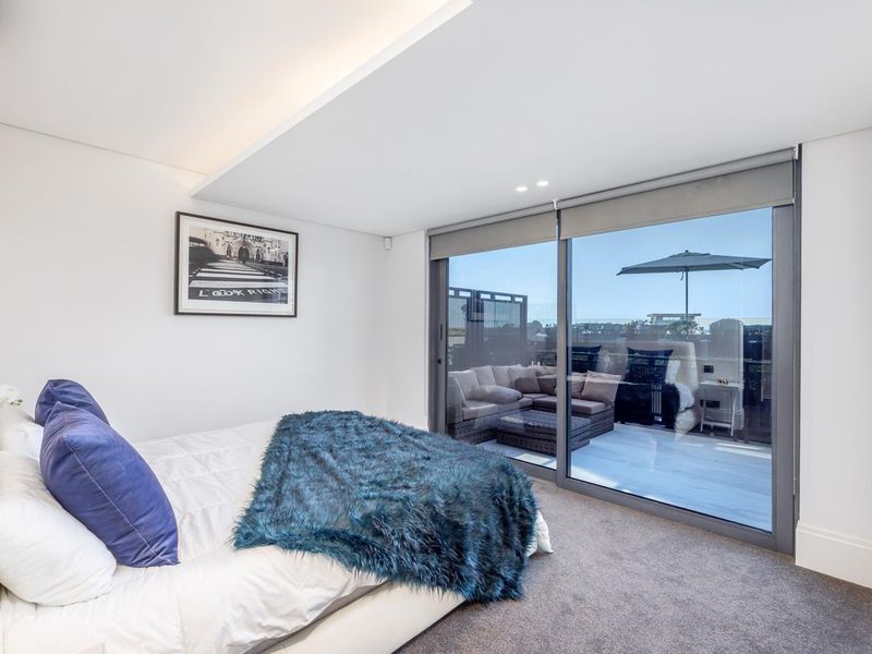 Modern bedroom featuring plush carpeting, recessed ceiling lighting, and large sliding glass doors providing seamless access to a private balcony.