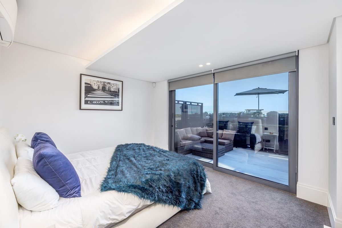 Modern bedroom featuring plush carpeting, recessed ceiling lighting, and large sliding glass doors providing seamless access to a private balcony.