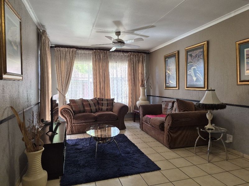 A comfortable living room featuring tiled flooring, a ceiling fan, and neutral wall tones, providing a functional and well-lit space for relaxation.