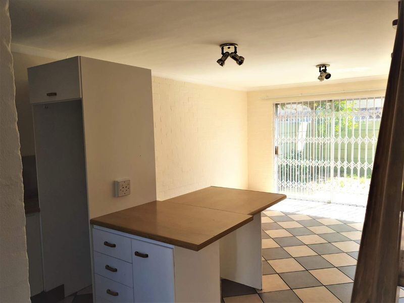 An open-plan living area featuring tiled flooring, built-in cabinetry, and a sliding door with a security gate leading to the exterior.