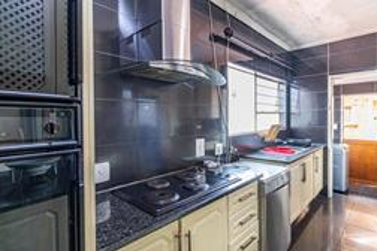 A functional kitchen featuring built-in appliances, dark tiled splashbacks, granite countertops, and ample fitted cabinetry with a view into an adjacent utility area.