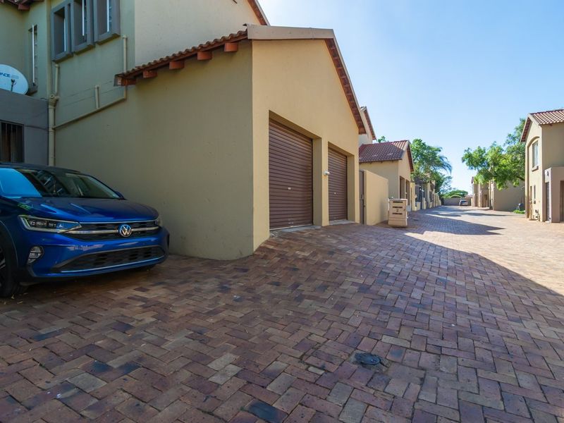 Exterior view of a townhouse complex featuring a paved driveway and double garage with roll-up doors.