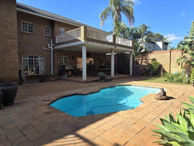 Rear exterior view featuring a swimming pool, paved patio area, and a covered ground-floor patio with an overhead balcony.
