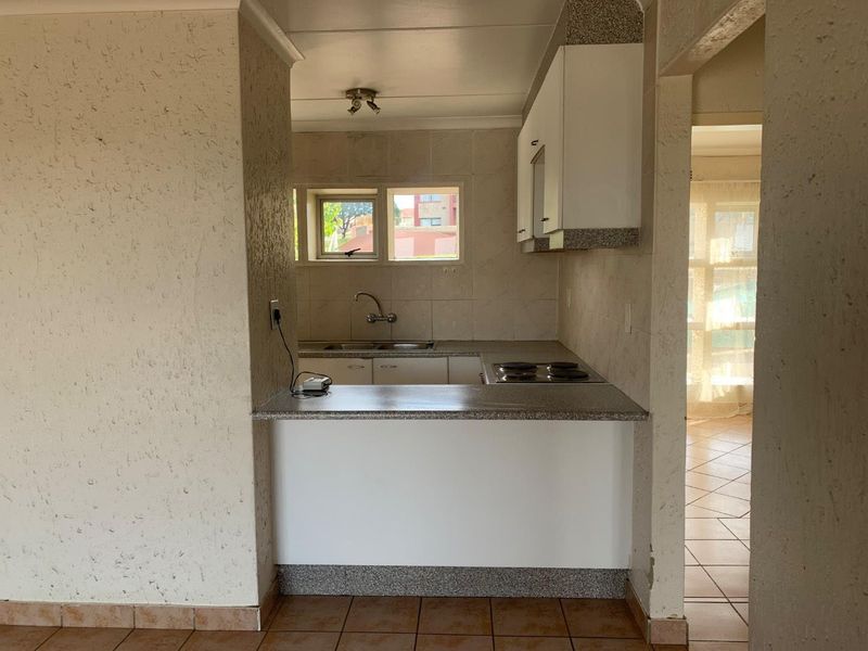 A functional kitchen featuring built-in cabinetry, laminate countertops, a stainless steel sink, and an electric hob, with tiled flooring and backsplash.