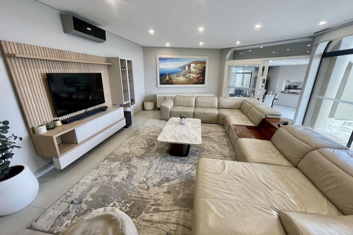 Spacious living room featuring a modern built-in media unit with timber slat detailing, recessed downlighting, and large glass sliding doors leading to the patio.