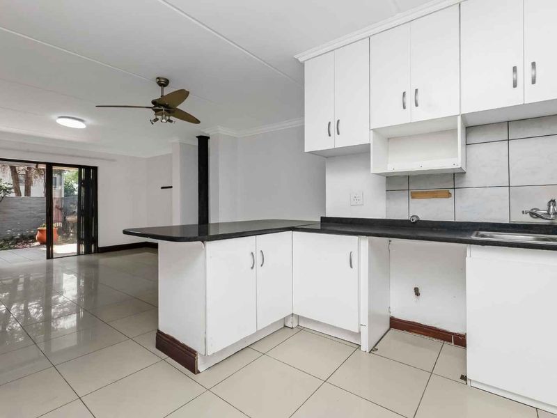 Open plan kitchen and living area featuring tiled floors, white cabinetry with granite countertops, and sliding door access to the outdoor space.