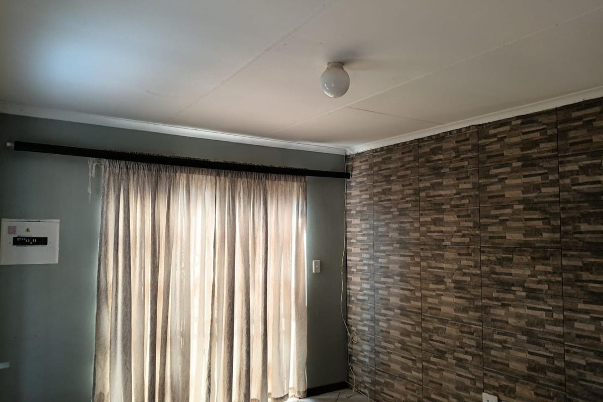 An empty living area featuring tiled flooring, a textured feature wall, and an integrated electrical distribution board.