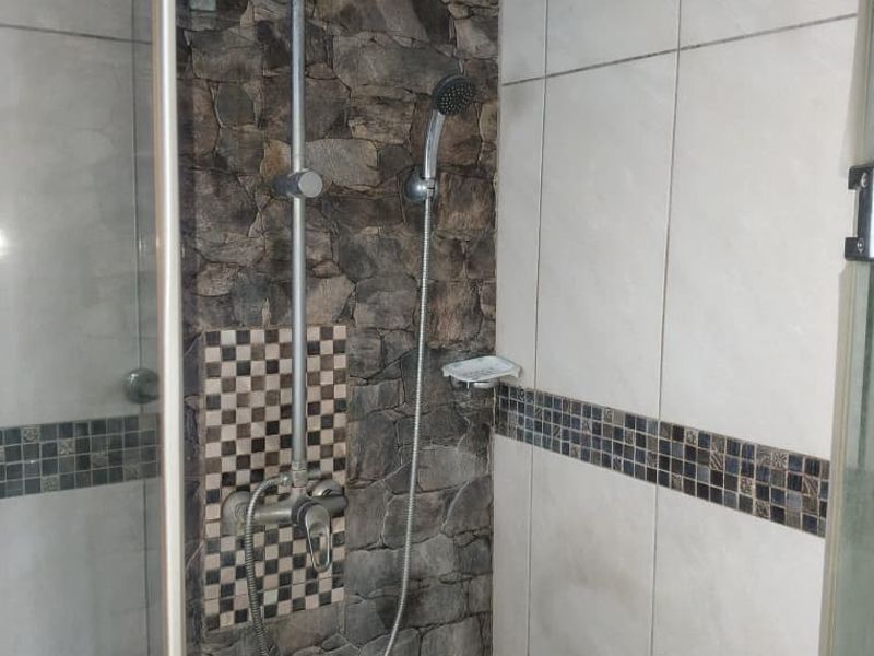 A shower enclosure featuring a rain shower head, handheld attachment, and decorative stone-look wall tiles with a mosaic accent border.