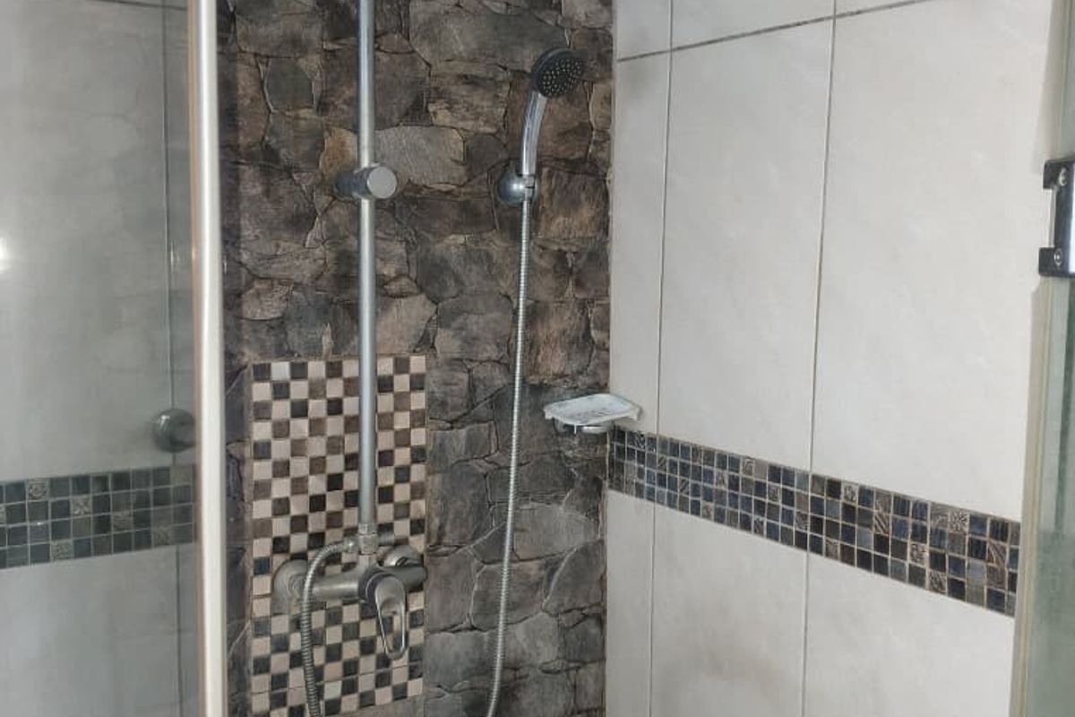 A shower enclosure featuring a rain shower head, handheld attachment, and decorative stone-look wall tiles with a mosaic accent border.