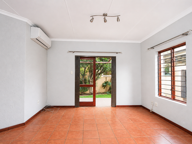 A bright, empty living room featuring terracotta floor tiles, an air conditioning unit, and direct access to the rear garden through a sliding glass door.