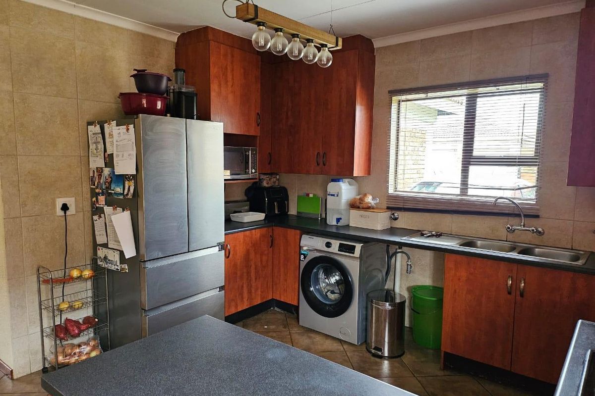 A functional kitchen featuring wooden cabinetry, laminate countertops, a double basin sink, and tiled finishes, providing a practical workspace for daily meal preparation.