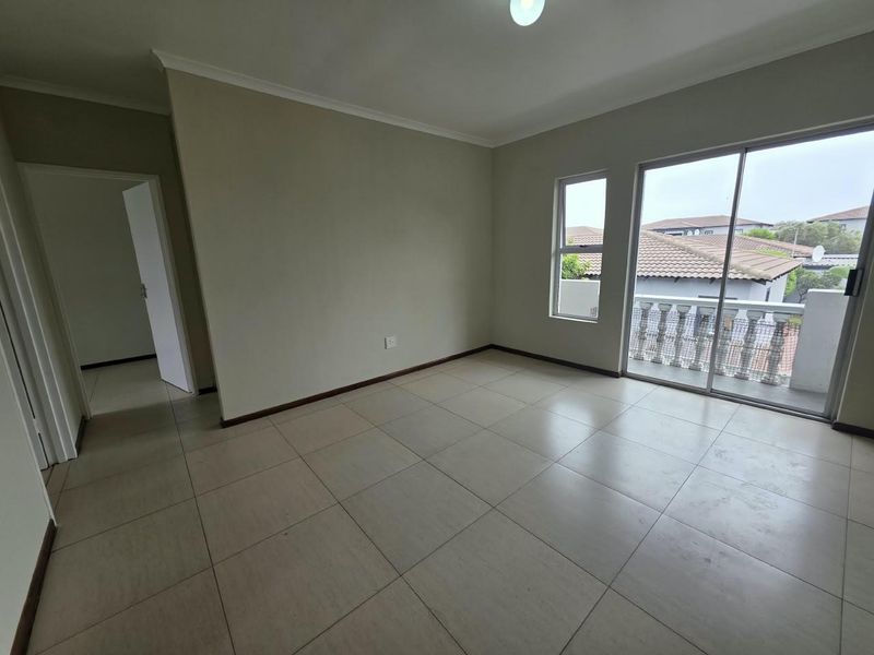 A bright, empty living area featuring neutral tiled flooring and a sliding glass door that opens onto a balcony.