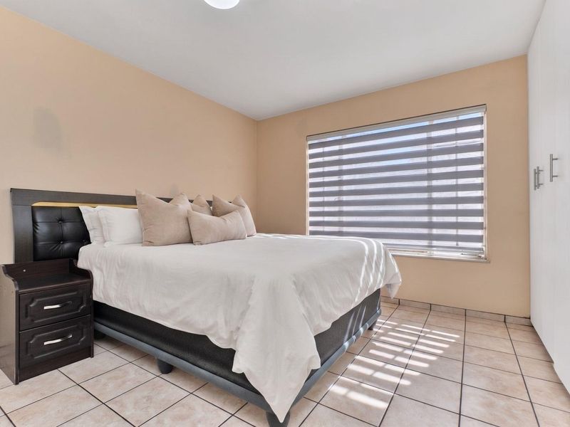 A well-maintained bedroom featuring neutral wall tones, tiled flooring, a built-in wardrobe, and modern zebra blinds for adjustable natural light.