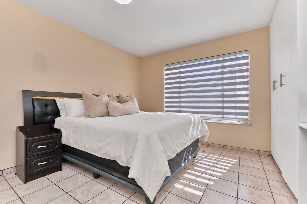 A well-maintained bedroom featuring neutral wall tones, tiled flooring, a built-in wardrobe, and modern zebra blinds for adjustable natural light.