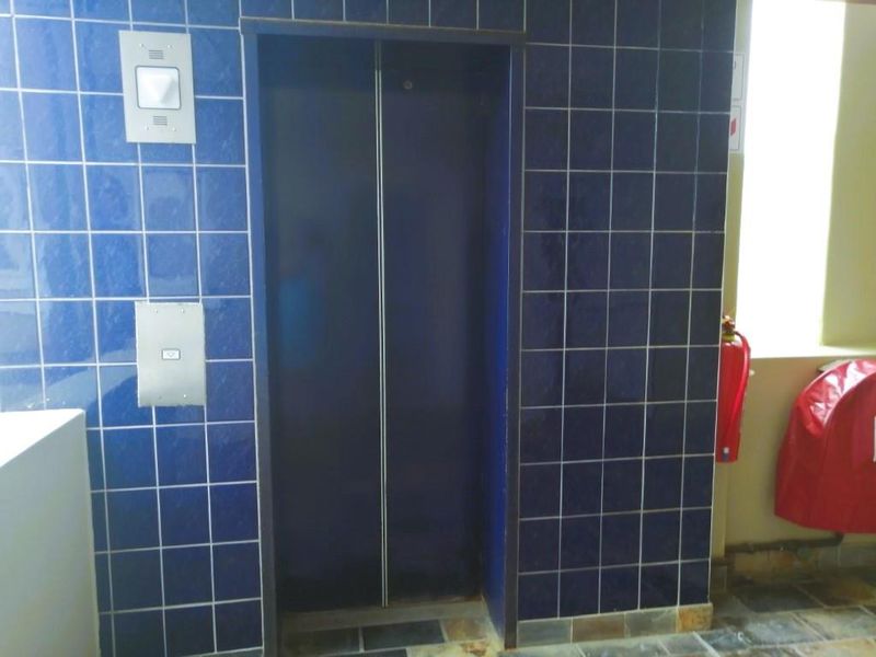 A functional apartment building elevator lobby featuring blue tiled walls and essential fire safety equipment.