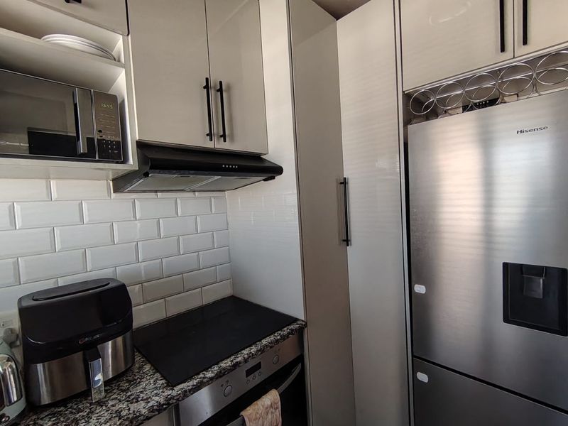 Modern kitchen featuring high-gloss cabinetry, granite countertops, subway tile backsplash, and integrated appliances including an oven, hob, and microwave.