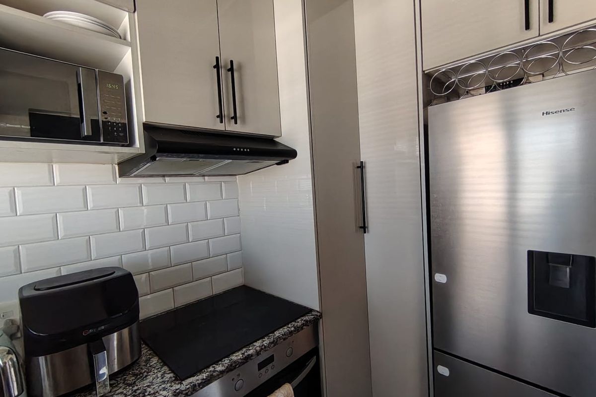 Modern kitchen featuring high-gloss cabinetry, granite countertops, subway tile backsplash, and integrated appliances including an oven, hob, and microwave.