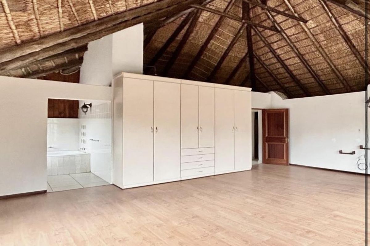 Spacious bedroom featuring a high vaulted thatch ceiling, laminate flooring, and extensive built-in cabinetry, with an adjoining en-suite bathroom area.