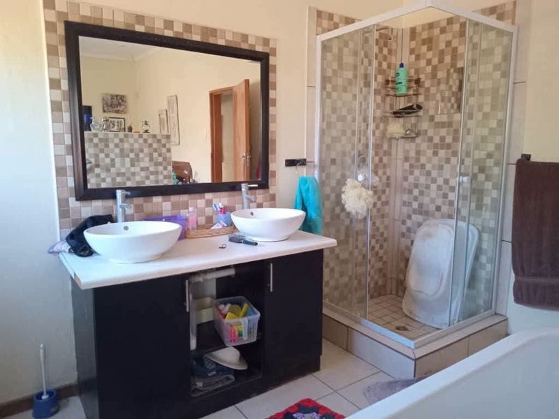 Bathroom featuring a double vanity with vessel sinks, a framed mirror, and a corner shower enclosure with tiled surround.