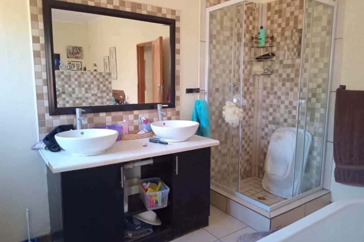 Bathroom featuring a double vanity with vessel sinks, a framed mirror, and a corner shower enclosure with tiled surround.
