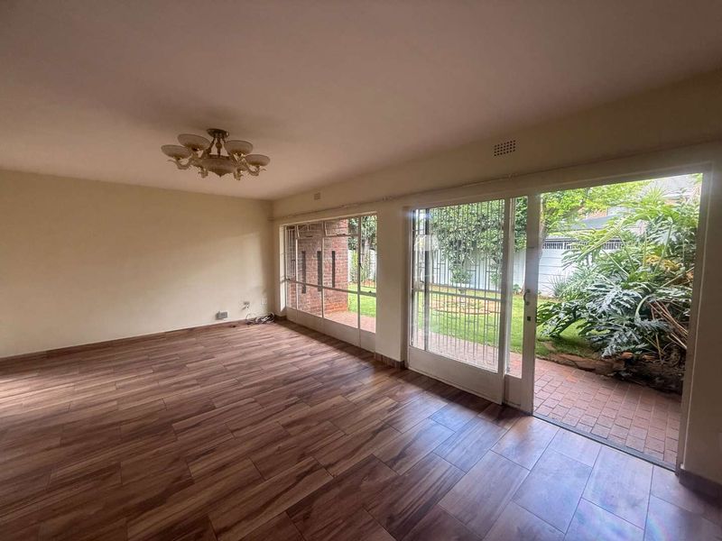 Spacious, empty living room featuring wood-look tile flooring and large sliding glass doors that open onto a private garden patio.