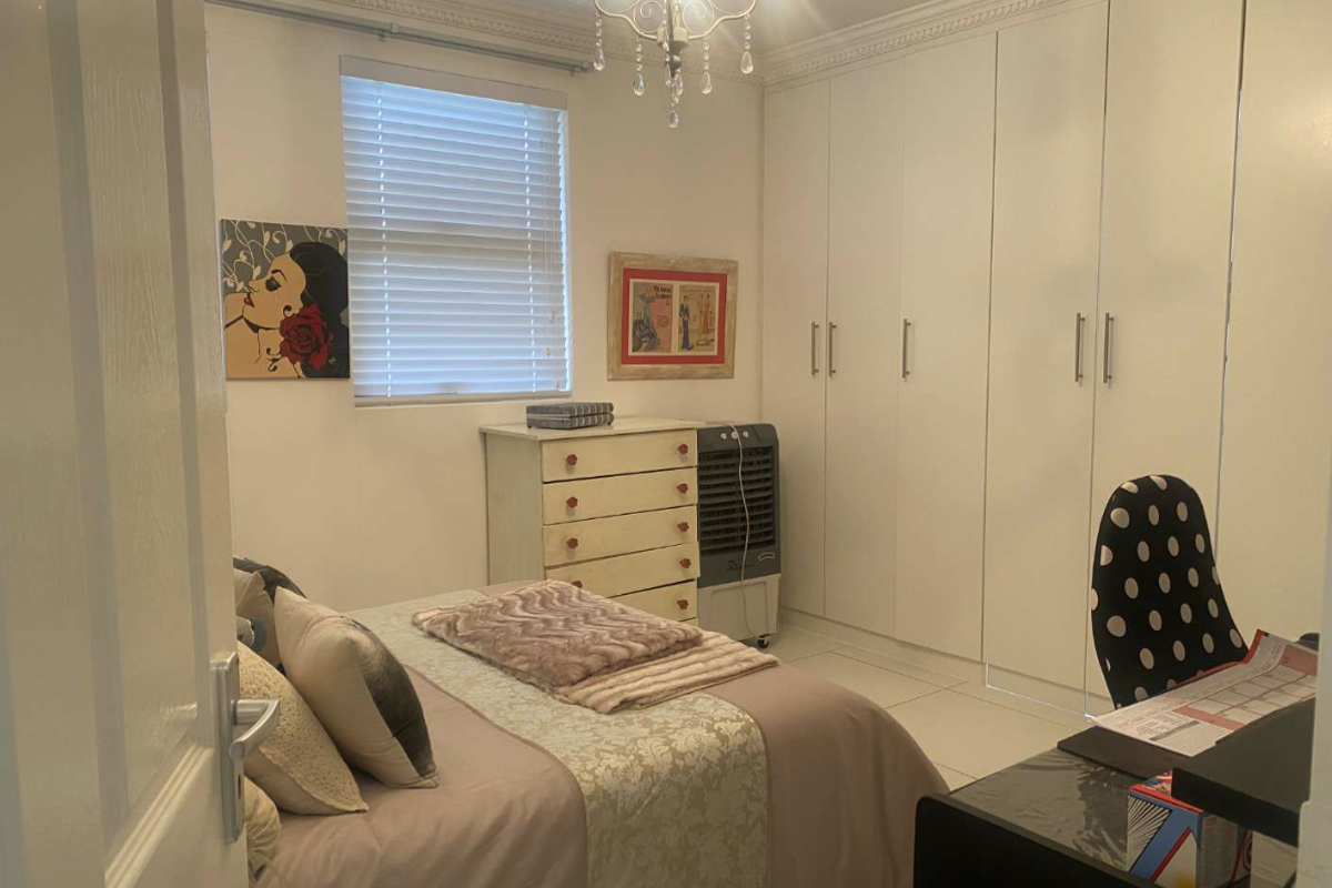 A well-maintained bedroom featuring extensive built-in cupboards, tiled flooring, and decorative ceiling cornice, offering ample storage and a clean, neutral aesthetic.