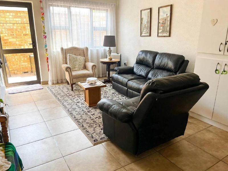 A bright living room featuring tiled flooring, large windows for natural light, and direct access to an outdoor area through a glass door.