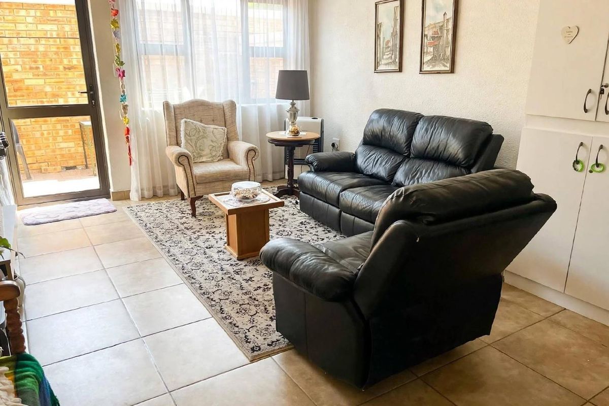 A bright living room featuring tiled flooring, large windows for natural light, and direct access to an outdoor area through a glass door.