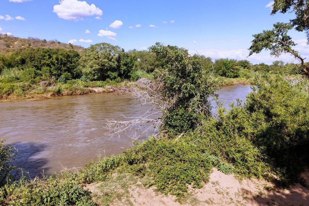 A scenic view of a natural river flowing through a lush, vegetated landscape, highlighting the tranquil and picturesque setting of the vacant land.