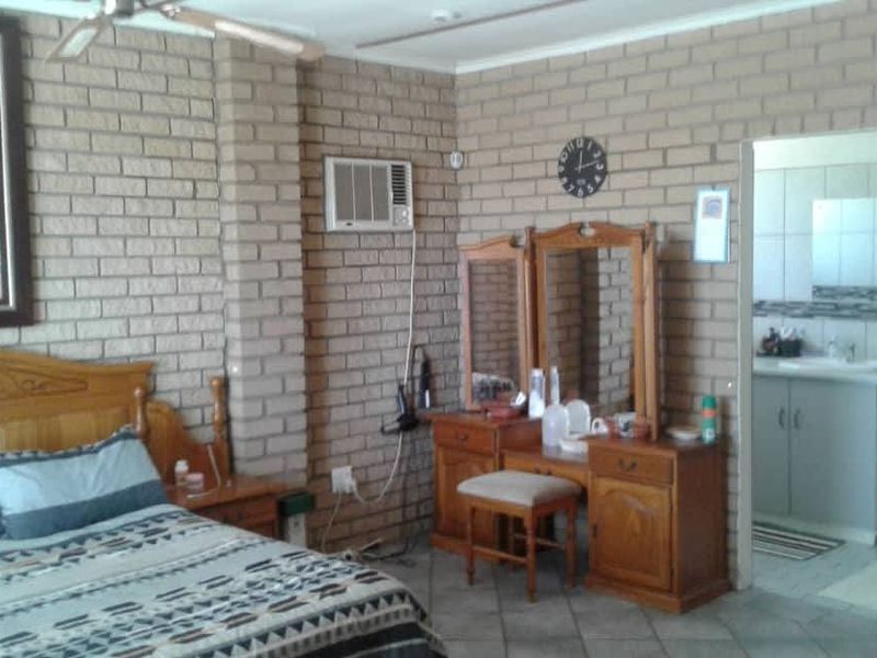 A bedroom featuring exposed brick walls, tiled flooring, a ceiling fan, and an integrated air conditioning unit, with direct access to an en-suite bathroom.