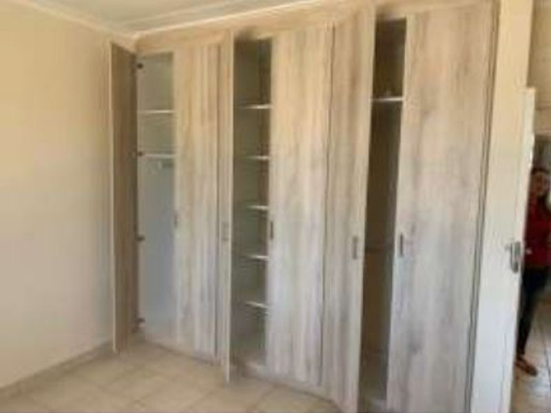 A bedroom featuring light wood-finish built-in cupboards and neutral tiled flooring, offering ample storage space.