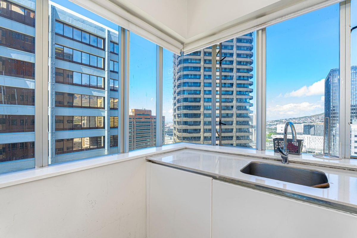 Compact kitchen area featuring stone countertops, undermount sink, and expansive floor-to-ceiling windows offering panoramic city views.