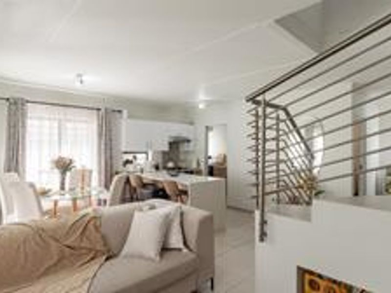 Modern open-plan living area featuring a sleek kitchen with island, tiled floors, and a contemporary stainless steel staircase railing.