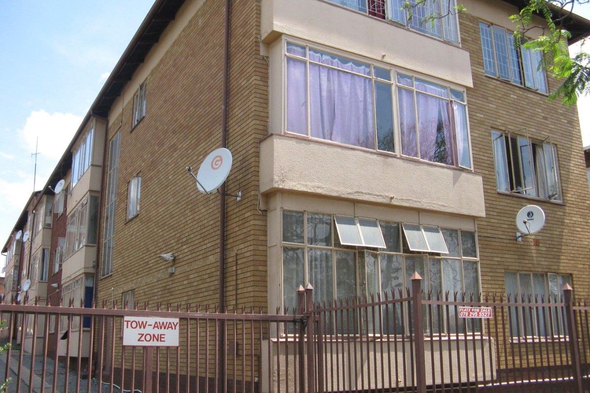 Exterior view of a multi-story apartment building featuring brick facade, metal security fencing, and multiple satellite dish installations.