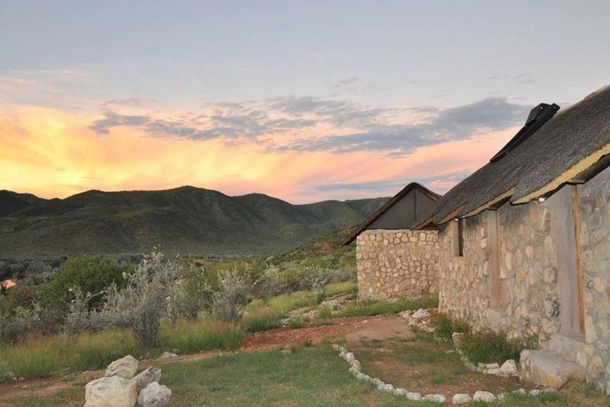 Exterior view of stone-clad lodge units featuring traditional thatched roofing, set against a scenic mountain landscape at sunset.