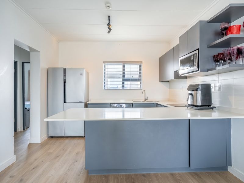 Modern kitchen featuring sleek grey cabinetry, white quartz countertops, integrated microwave, and durable laminate flooring with a functional breakfast bar layout.