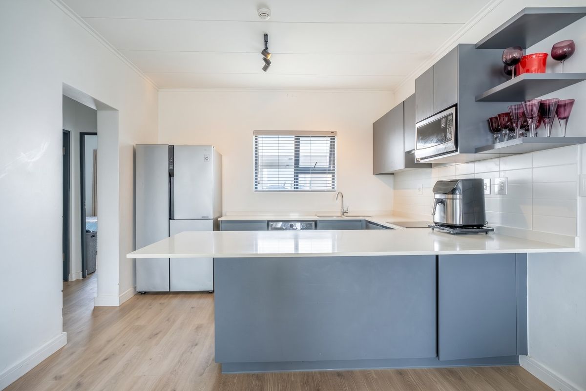 Modern kitchen featuring sleek grey cabinetry, white quartz countertops, integrated microwave, and durable laminate flooring with a functional breakfast bar layout.
