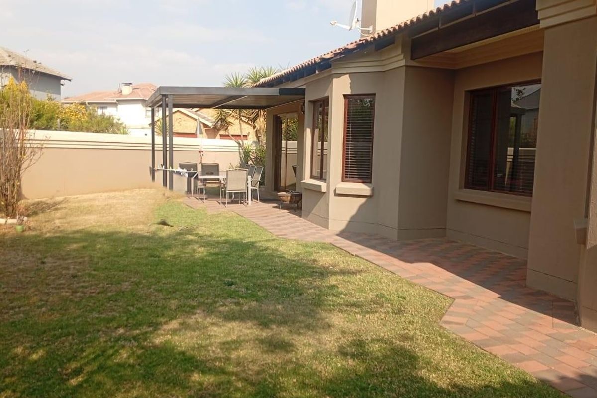 Rear exterior view of the house featuring a paved patio area, covered pergola, and a private garden with boundary walling.