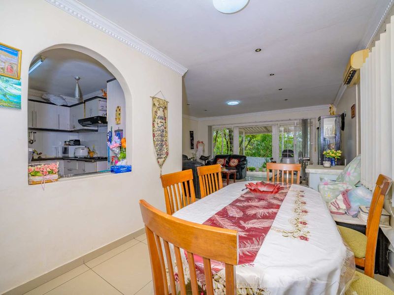 Open-plan dining and living area featuring tiled floors, crown molding, and an arched serving window connecting to the kitchen, with access to a patio.