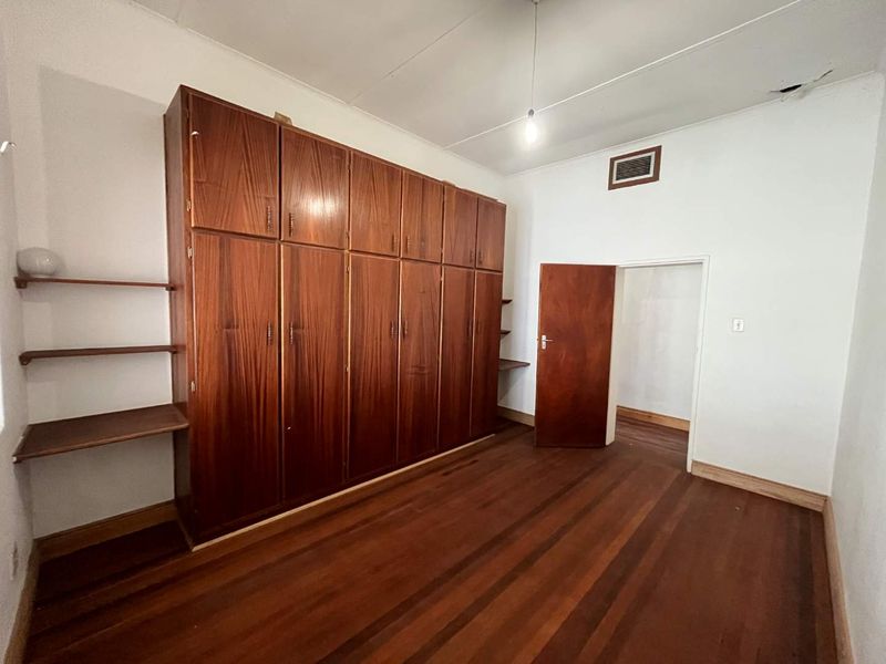 A bedroom featuring original wooden flooring and extensive built-in wooden cabinetry, offering ample storage space in a classic layout.