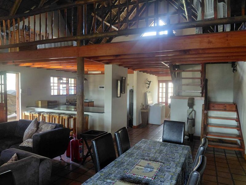 Spacious open-plan living and dining area featuring exposed timber beams, a mezzanine level, and a rustic thatched roof design.