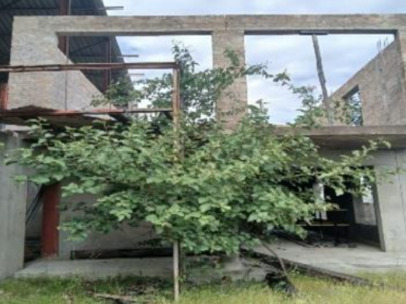 An unfinished industrial building structure featuring exposed brickwork, concrete columns, and a steel roof frame, currently in a state of incomplete construction.