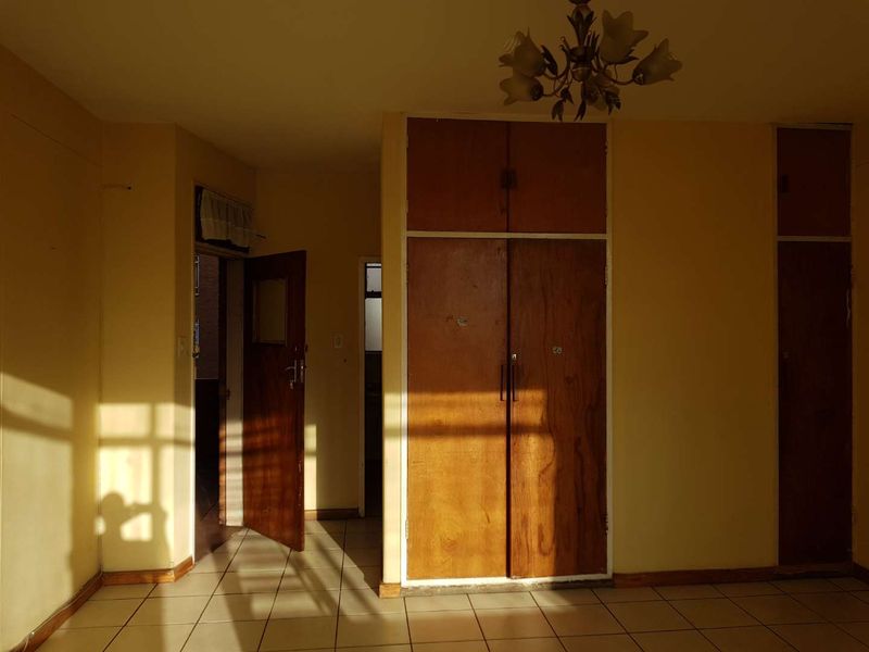 An empty bedroom featuring tiled flooring and built-in wooden cupboards, requiring cosmetic updates to modernize the space.